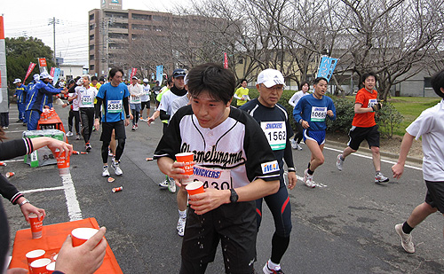 ソフトボール部員がボランティアしている給水所でスポーツドリンクを補給する丸亀工場の桑田和宏さん