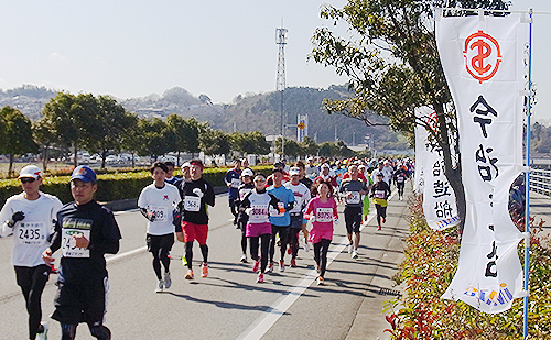 今治造船のノボリの横をそれぞれのペースで走る愛媛マラソンのランナー