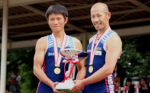 表彰台の頂上で優勝カップを持つ井出・別府両選手